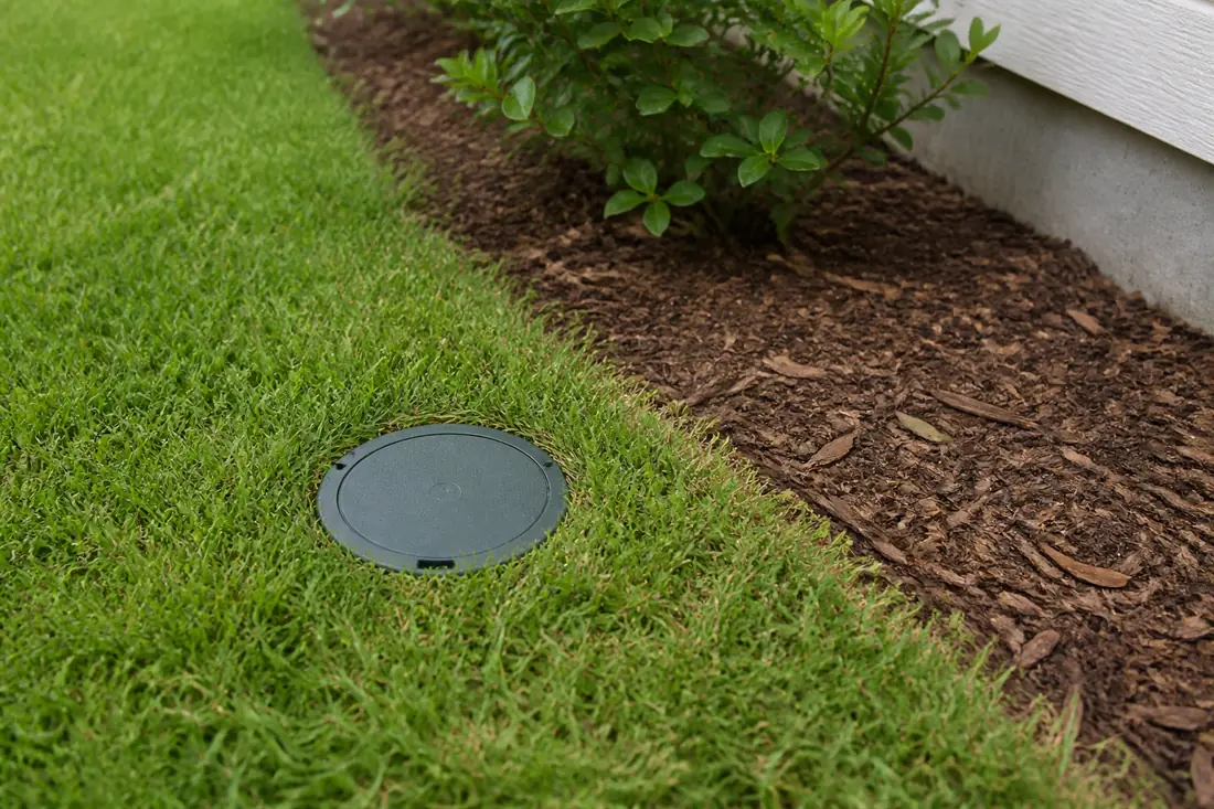 An in-ground termite bait station set into a lawn beside a foundation