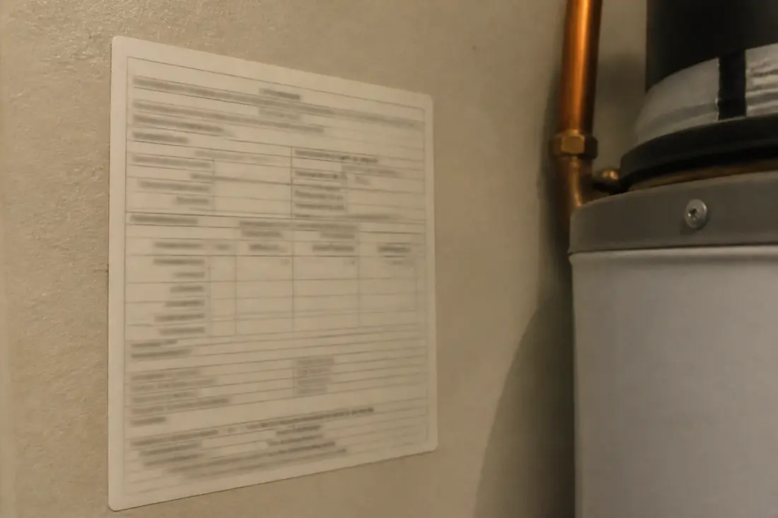 A small printed service sticker on the wall beside a water heater showing treatment details