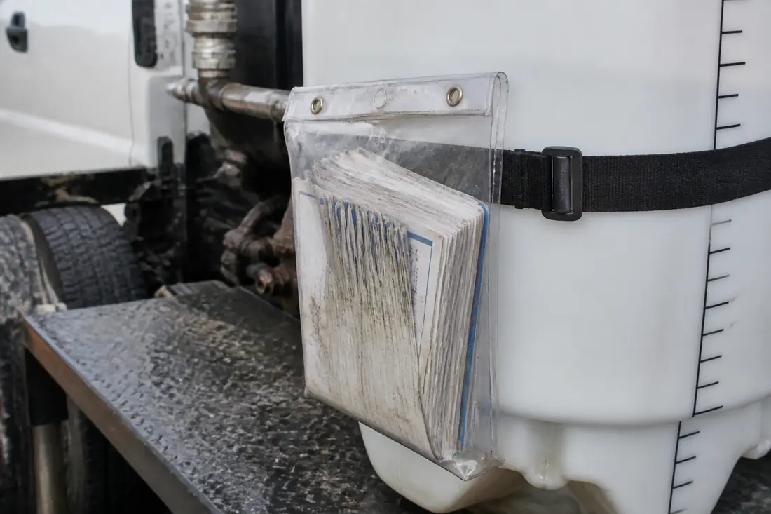 A plastic document pouch holding a folded label booklet strapped to a sprayer tank